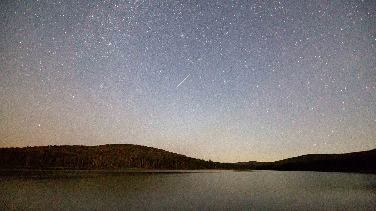 Meteor over a dark lake and forested ridgeline in northern New Hampshire