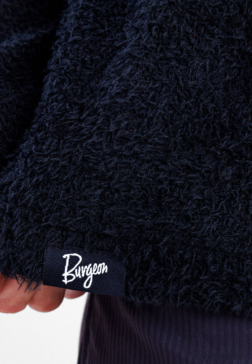 Close-up of a black Alpha 90 hoodie with a small black fabric label reading Burgeon, held by a hand.