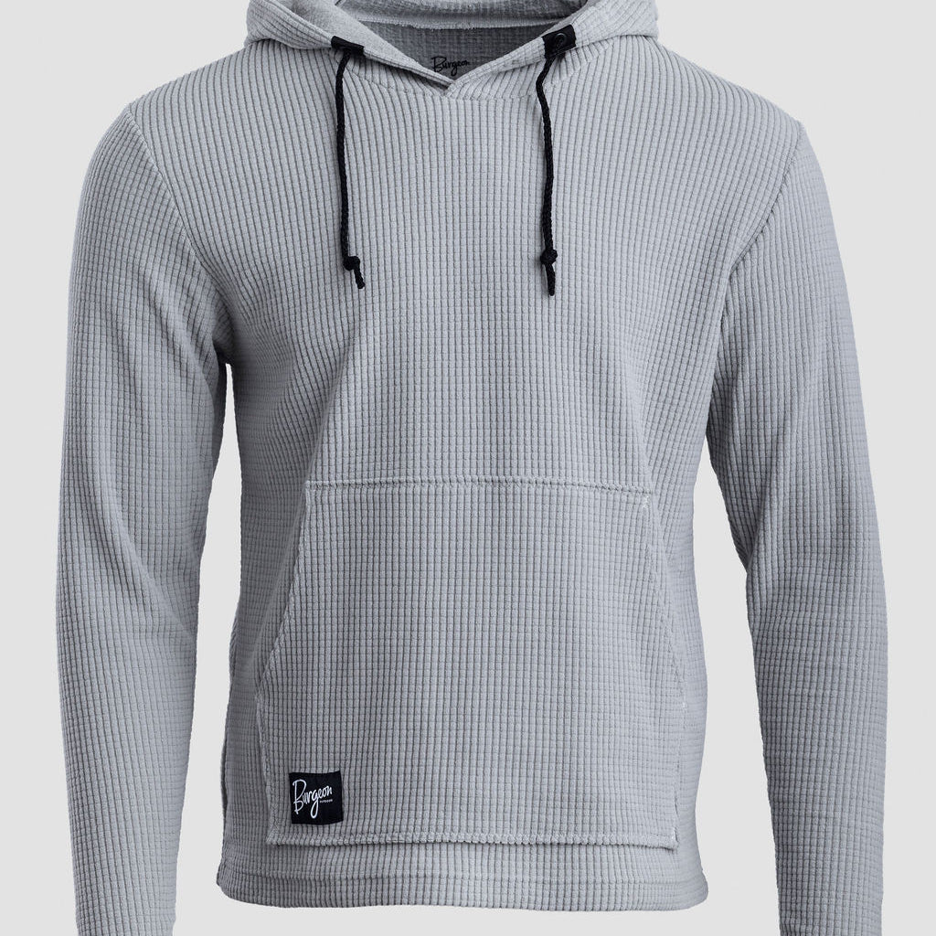 A light gray Highlander hoodie with black drawstrings and a small black brand patch on the lower front pocket, shown against a light gray background.
