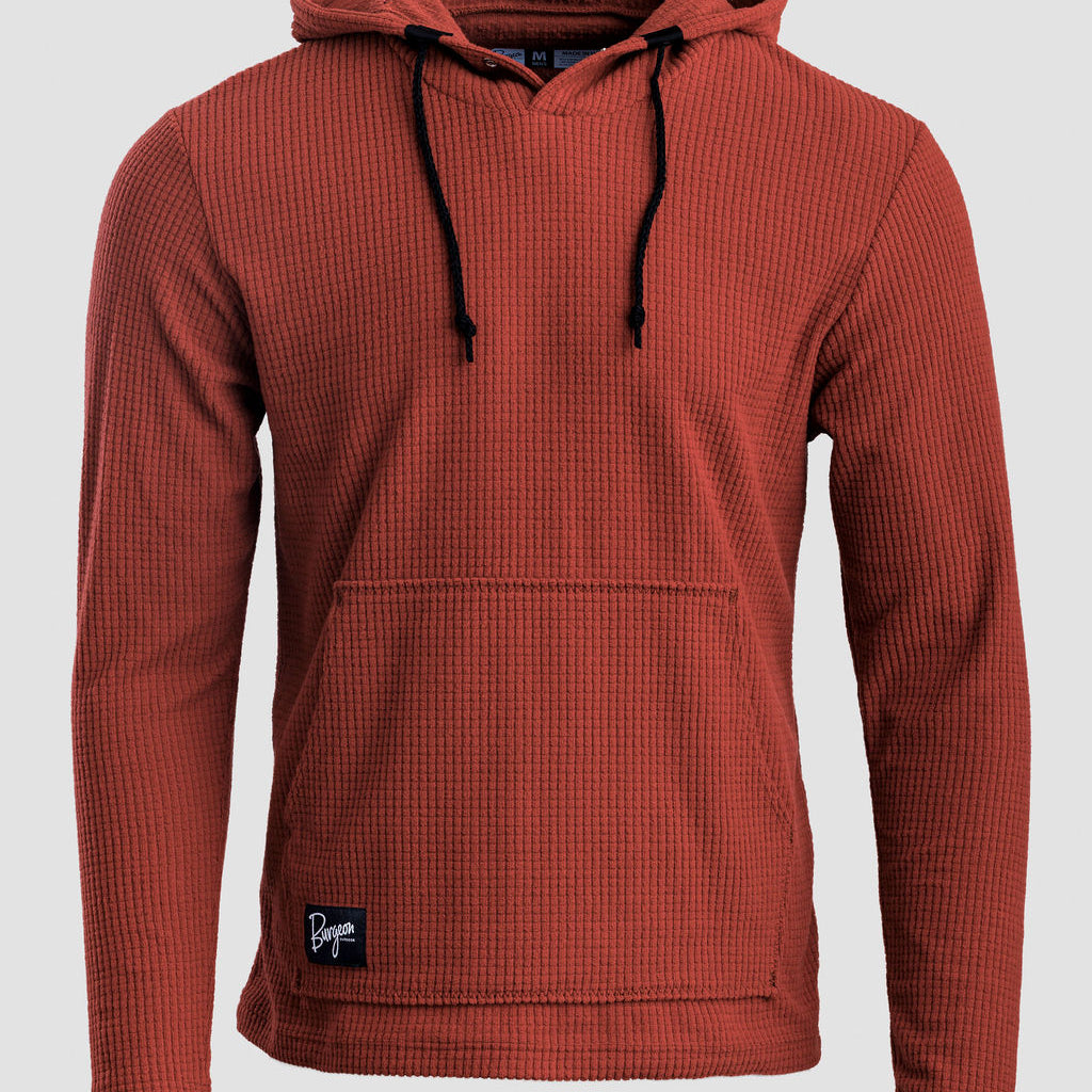 A rust-colored Highlander hoodie with black drawstrings and a small black brand patch on the lower left hem, shown against a light gray background.
