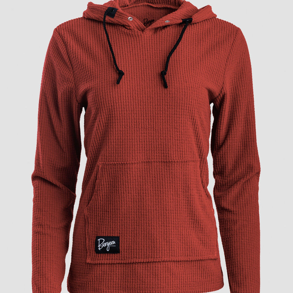 A rust-colored Highlander hoodie with black drawstrings and a small black brand patch on the front pocket, shown against a light gray background.