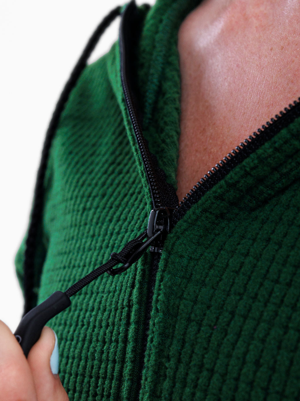Close-up of a person wearing a textured green zip-up hoodie, pulling the black zipper tab open with one hand.