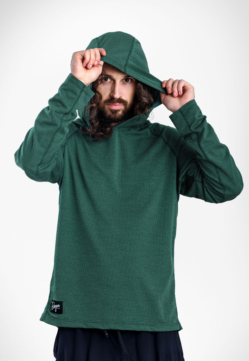 A man wearing a dark green Sunseeker Hoodie with a textured knit pattern, holding up the hood with both hands against a plain white studio background.