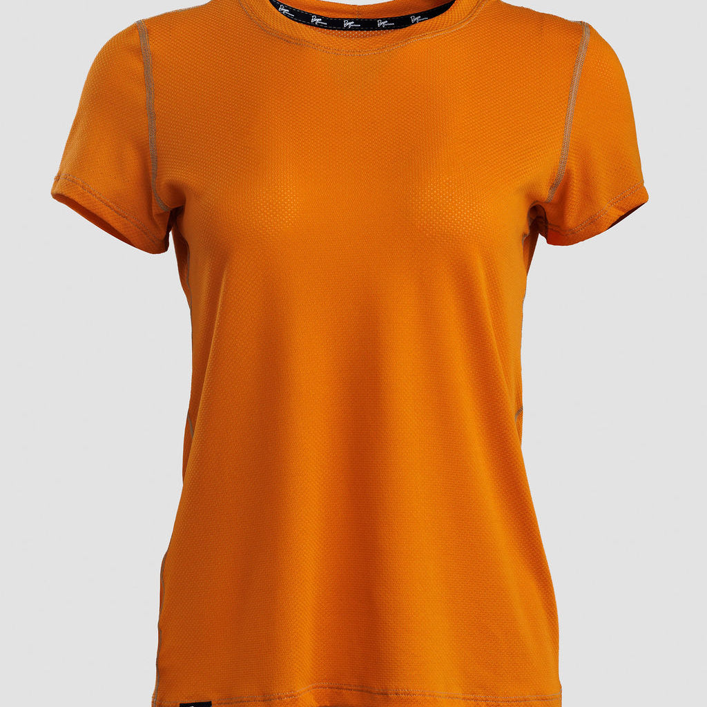 An orange short-sleeve crewneck athletic t-shirt with subtle gray piping details along the shoulders and a small black logo patch near the bottom hem, displayed on a neutral light gray background.