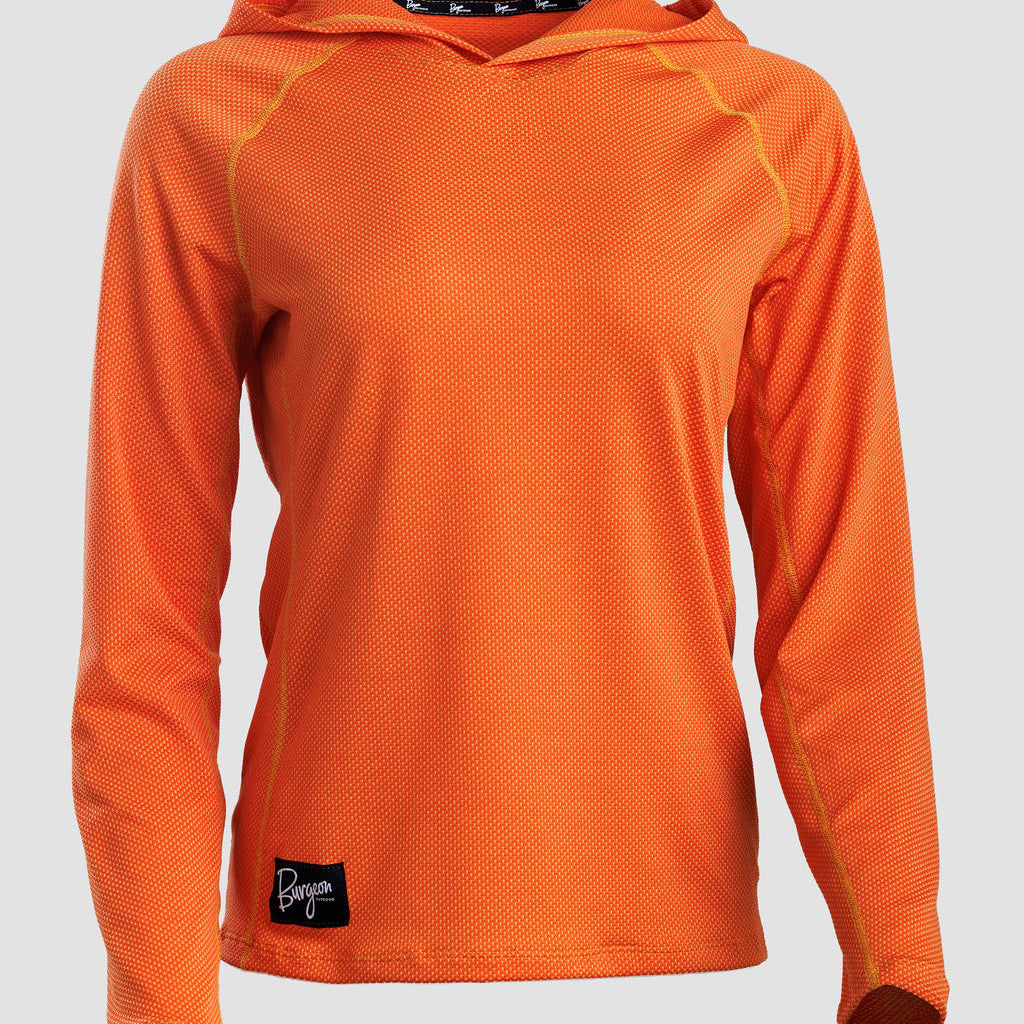 An orange long-sleeve sun hoodie with a textured mesh fabric, raglan sleeves, and a small black logo patch on the lower left hem, shown against a light gray background.