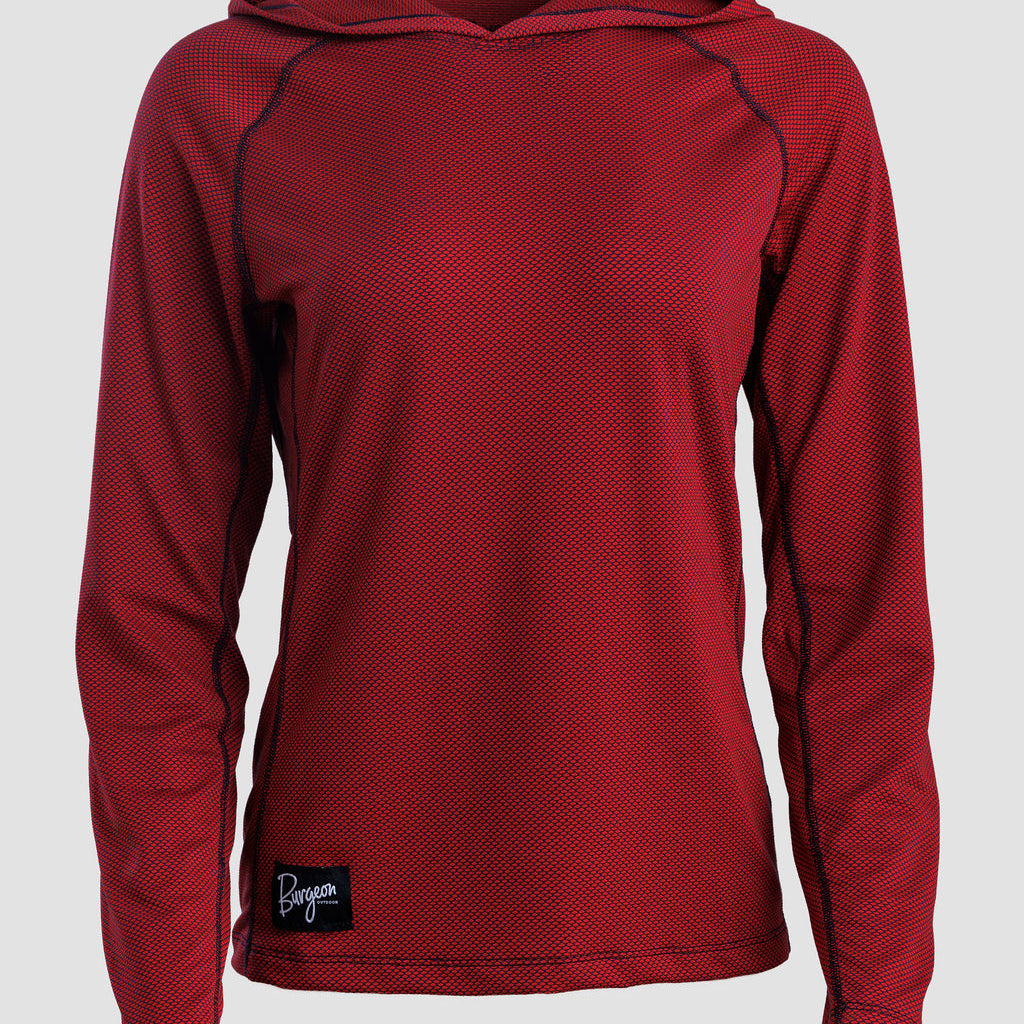 A women's long-sleeve sun hoodie in a deep red or burgundy color, featuring a textured mesh fabric and a small black brand patch near the bottom hem, shown against a light gray background.