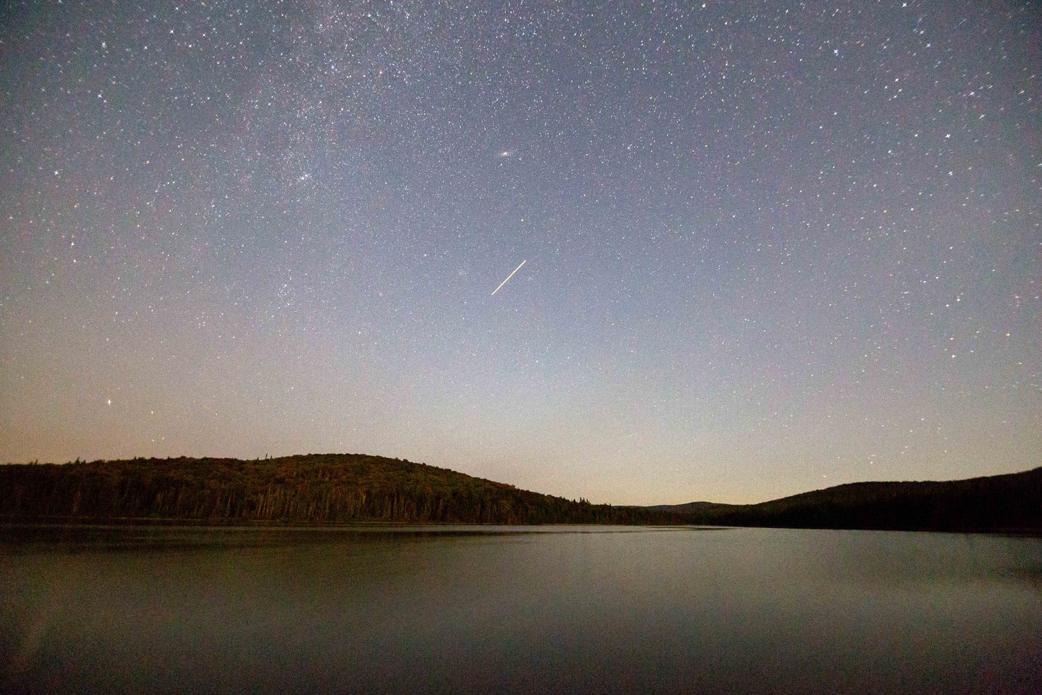 Meteor over a dark lake and forested ridgeline in northern New Hampshire