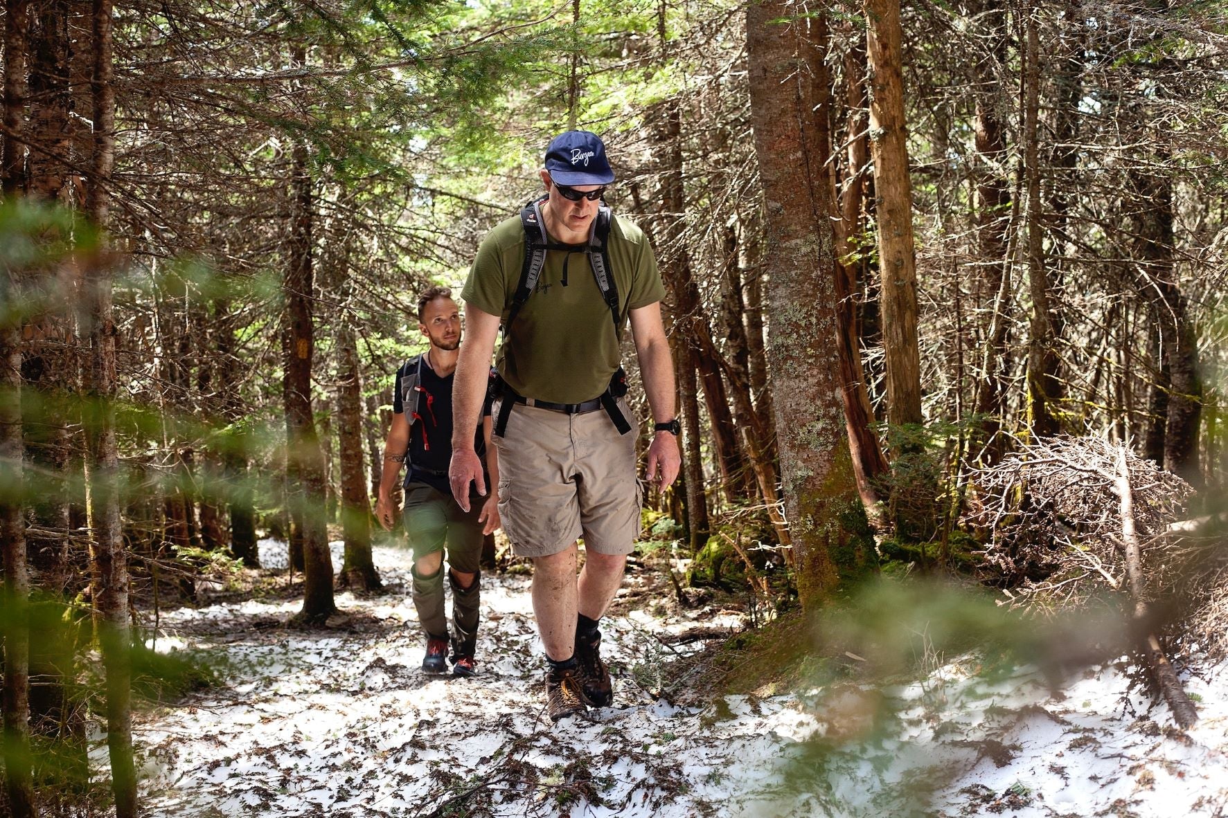 Two hikers trek up a snowy trail, one wearing the Delta Cool Tech T-Shirt and a Burgeon Ball Cap in 'Pacific Blue.'