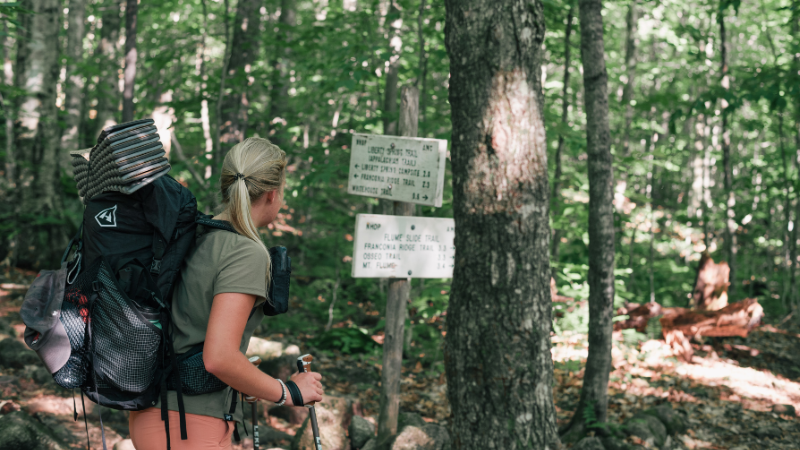 A female hiker approaches a trailhead while wearing a Burgeon Outdoor tech t-shirt.