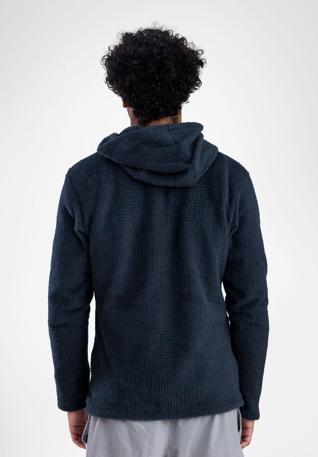 A man viewed from behind wearing a dark navy Alpha 120 hoodie, paired with light gray pants, against a plain light gray background.