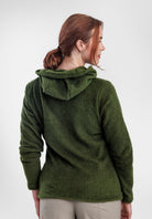 A woman shown from the back wearing a Alpha 120 Hoodie, paired with light beige pants, against a plain light gray studio background.