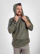 A man wearing a textured olive Alpha 60 hoodie and light gray pants, posing with the hood up against a light gray studio background.