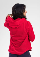 A woman shown from the back wearing a bright red textured hooded Alpha fleece hoodie photographed against a plain light gray studio background.