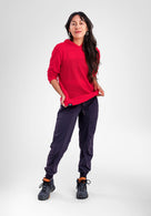A woman modeling a bright red long-sleeve hoodie and dark navy jogger pants with black hiking boots, standing against a light gray studio background.