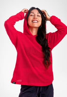 A woman wearing a bright red textured Alpha fleece hoodie with the hood up, posing against a light gray studio background.