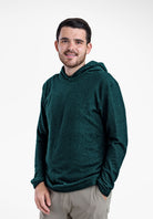 A man wearing a dark green textured Alpha 90 hoodie and light gray pants, standing against a plain white studio background.