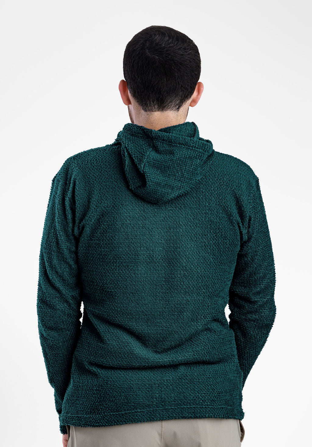A man viewed from behind wearing a textured dark green Alpha 90 hoodie  and light beige pants against a plain white studio background.