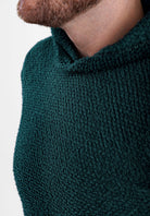 Close-up of a man wearing a dark green Alpha 90 hoodie, showing his neck and chin against a plain gray background.
