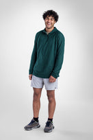 A man wearing a dark green quarter-zip Polartec Alpha Direct Hoodie, white athletic shorts, and gray running shoes, standing against a light gray studio background.