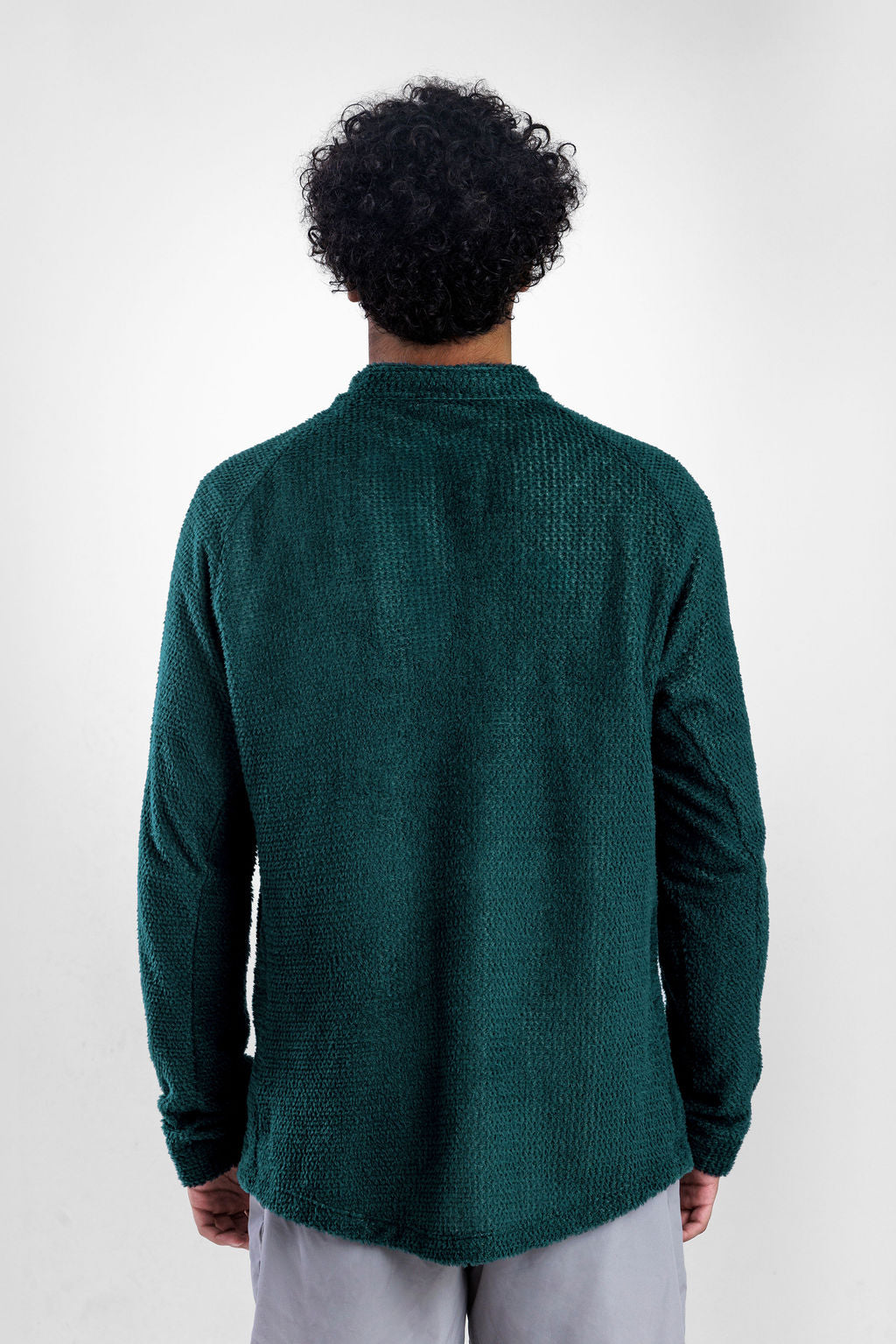 A man viewed from behind wearing a dark green Polartec Alpha Direct Hoodie and light gray pants, standing against a light gray studio background.