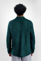 A man viewed from behind wearing a dark green Polartec Alpha Direct Hoodie and light gray pants, standing against a light gray studio background.