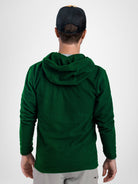 A man viewed from behind wearing a dark green Highlander fleece hoodie, a black baseball cap, and light gray pants, against a plain light gray studio background.