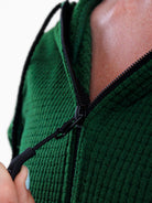 Close-up of a person wearing a textured green zip-up hoodie, pulling the black zipper tab open with one hand.