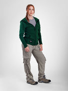 A woman modeling a dark green zip-up fleece jacket, paired with light gray cargo pants and hiking boots, against a light gray studio background.