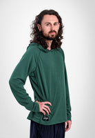 A man with long curly brown hair and a beard wearing a dark green long-sleeve Sunseeker Hoodie with a small black logo patch on the hem, posed against a light gray studio background.