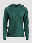 A dark green long-sleeve sun hoodie with a textured, mesh-like fabric, shown on a neutral light gray background. A small black brand patch is visible on the bottom left hem.