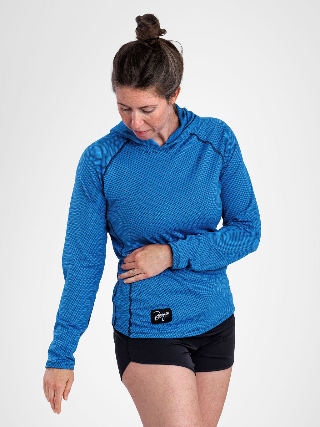 A woman wearing a bright blue long-sleeve sun hoodie and black athletic shorts, standing against a light gray studio background.