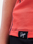Close-up of a coral-red textured athletic top with black contrast stitching and a black brand patch reading Burgeon.