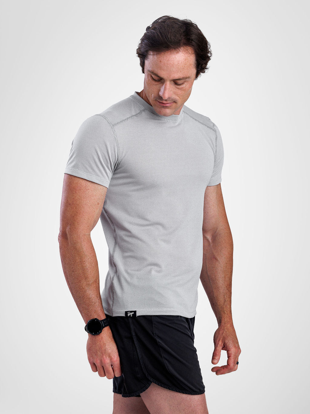 A man wearing a light gray athletic short-sleeve t-shirt and black athletic shorts, standing against a light gray studio background.