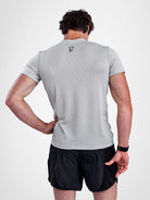 A man shown from the back wearing a light gray athletic t-shirt with a small black logo on the upper back and black athletic shorts, against a plain light gray studio background.