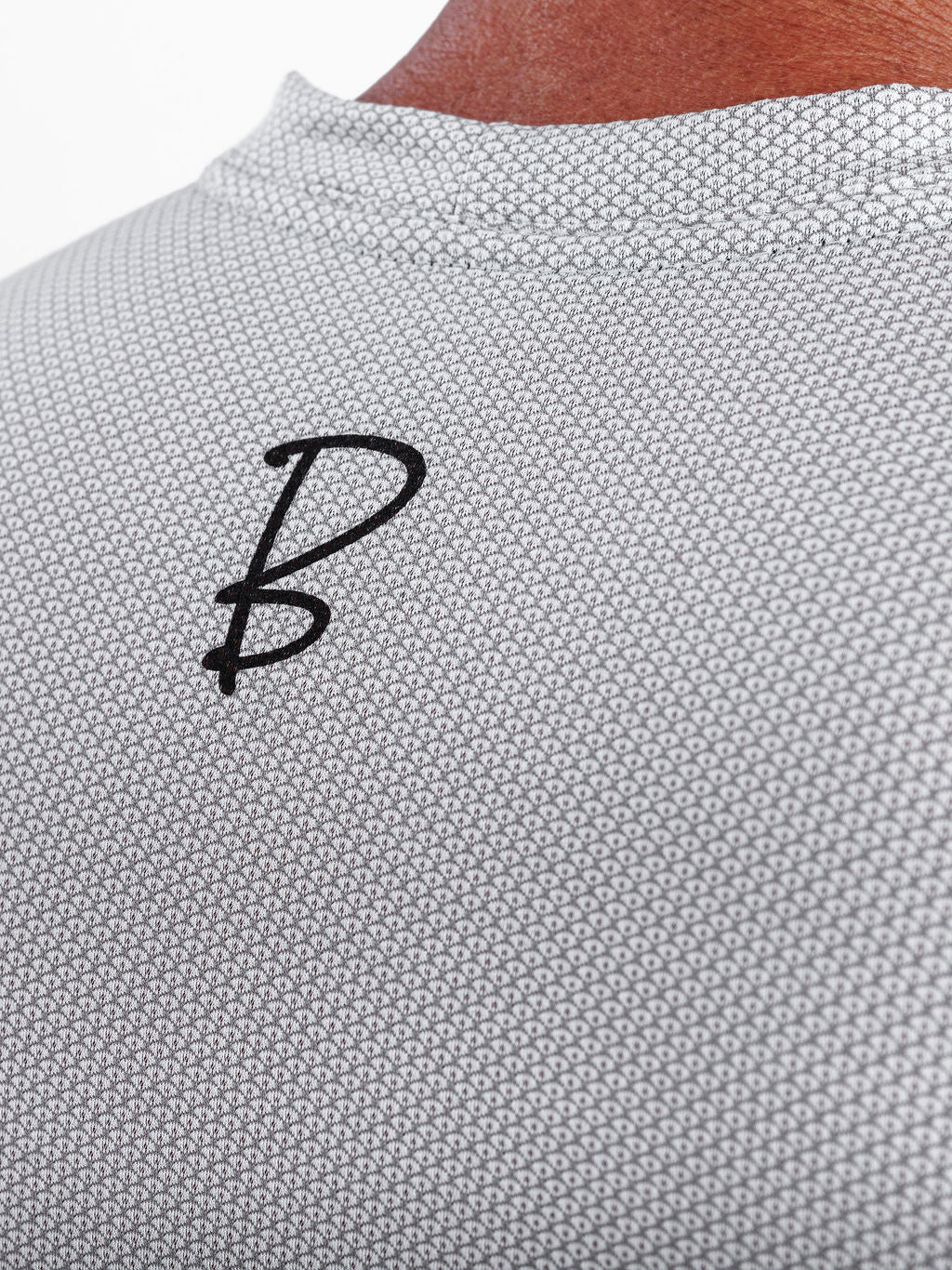 Close-up of a light gray textured knit top with a black stylized 'B' logo on the upper back, worn by a model.