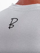 Close-up of a light gray textured knit top with a black stylized 'B' logo on the upper back, worn by a model.