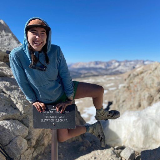 Hiker wearing Women's Iceberg Highlander Hoodie while leaping atop trailhead sign