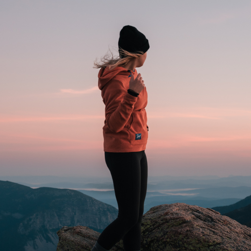 Hiker wearing Women's Orange Rust Highlander Hoodie atop mountain while looking off into the distance